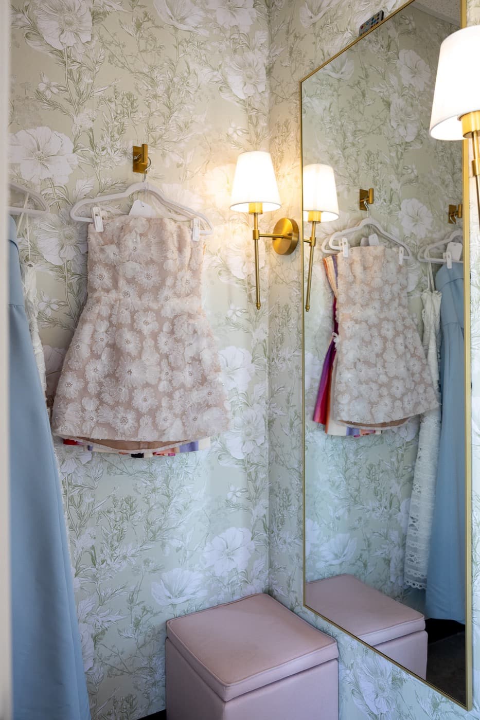 The floral fitting room with a gold sconce and mirror
